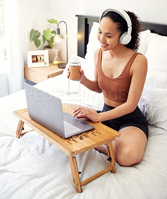 Buy stock photo Shot of a young woman using a laptop while sitting on her bed at home