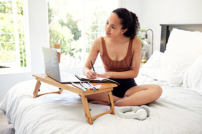 Buy stock photo Shot of a young woman using a laptop while writing in a notebook at home