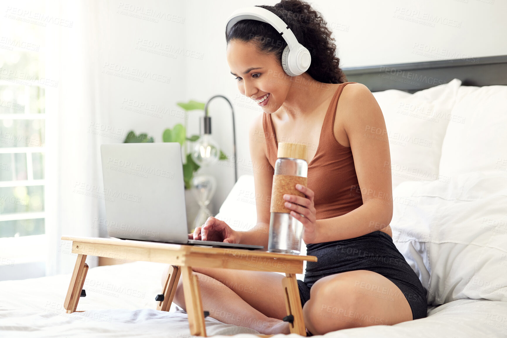 Buy stock photo Shot of a young woman using a laptop while sitting on her bed at home