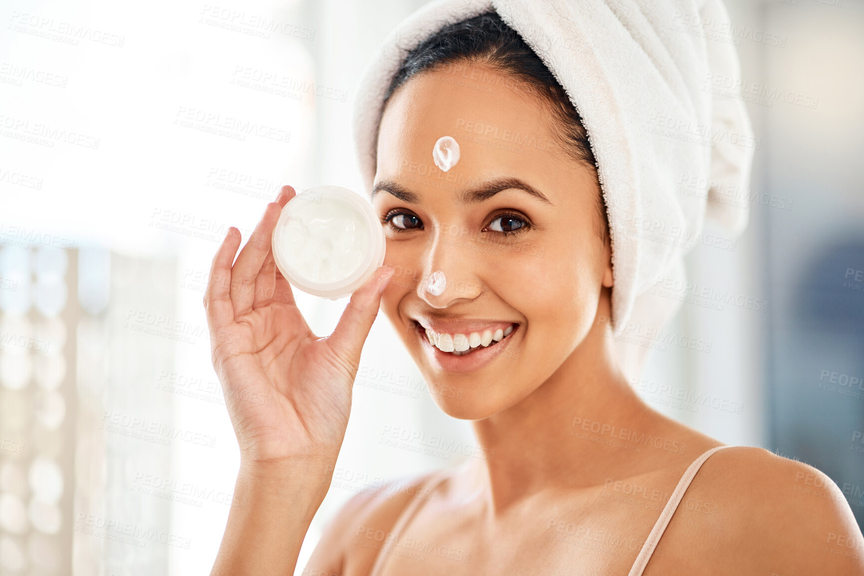 Buy stock photo Shot of a young woman applying cream to her face at home