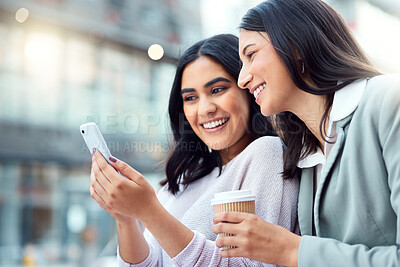 Buy stock photo Shot of two young businesswomen using a smartphone against an urban background