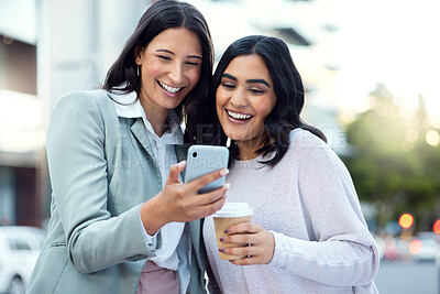 Buy stock photo Shot of two young businesswomen using a smartphone against an urban background