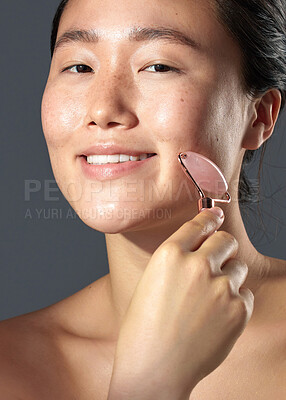 Buy stock photo Studio shot of a beautiful young woman using a face roller on her skin