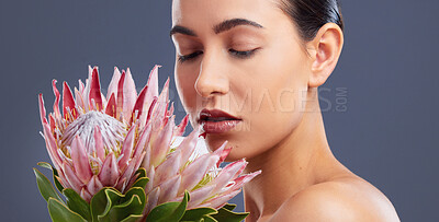Buy stock photo Studio shot of a beautiful young woman posing with proteas against a grey background