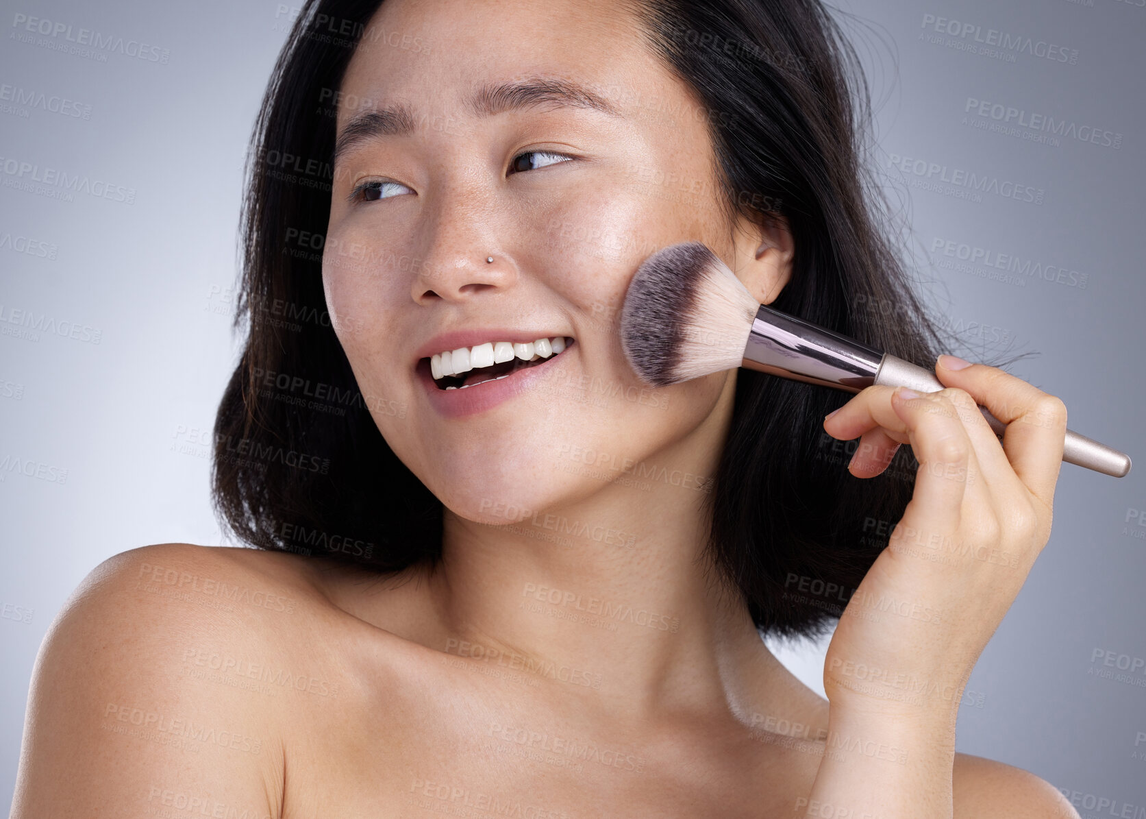 Buy stock photo Shot of a young woman applying makeup against a grey background