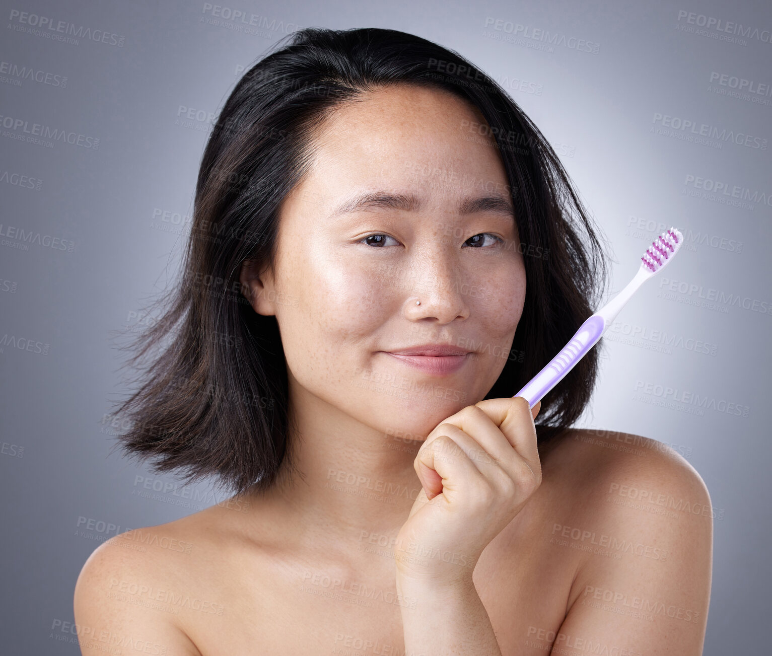 Buy stock photo Shot of a young woman holding a toothbrush against a grey background