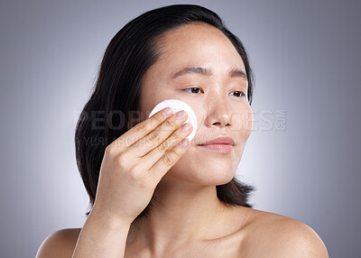 Buy stock photo Shot of a young woman using a cotton wipe on her face against a grey background