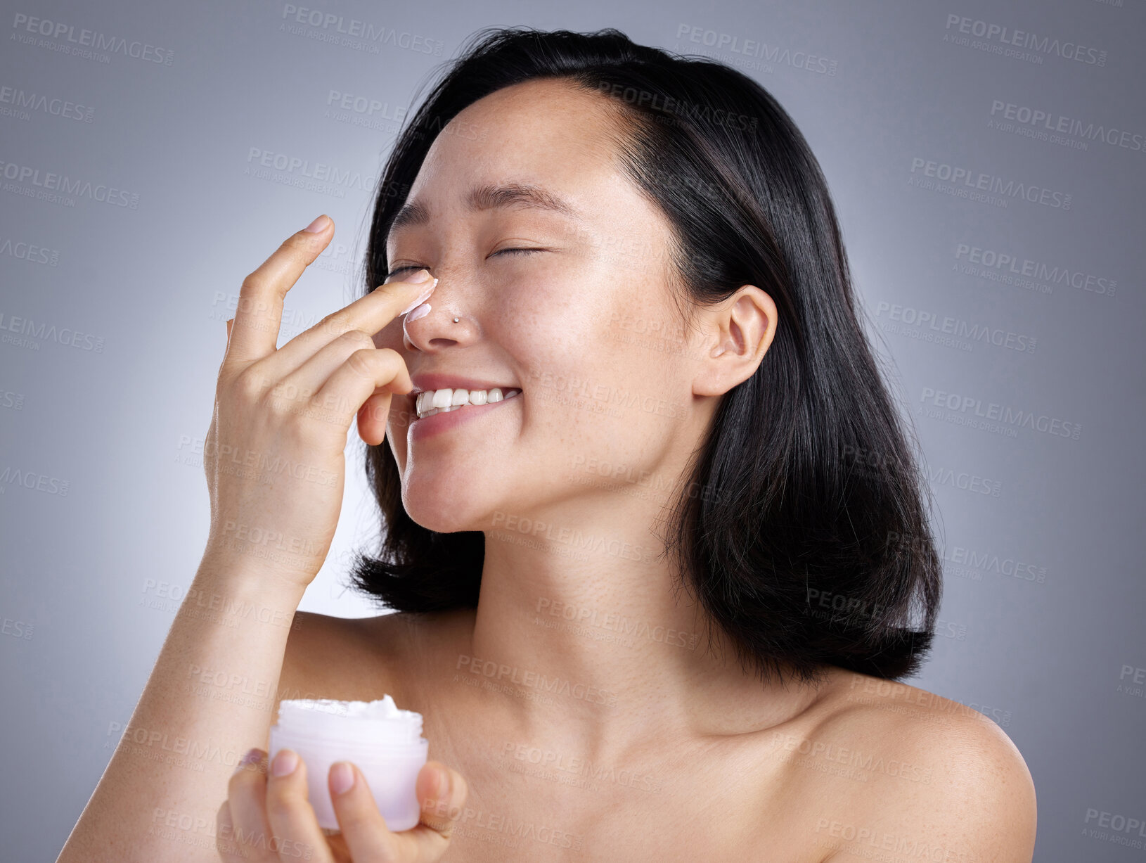 Buy stock photo Shot of a young woman applying lotion against a grey background