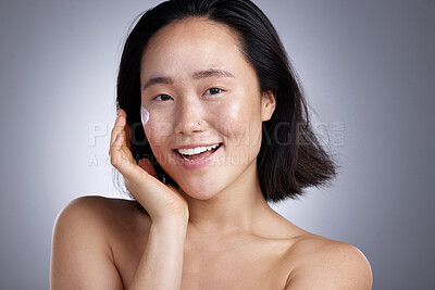 Buy stock photo Shot of a young woman applying lotion against a grey background