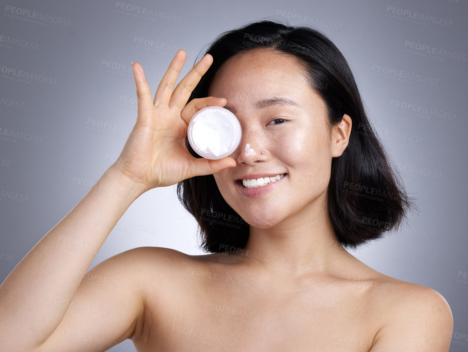 Buy stock photo Shot of a young woman applying lotion against a grey background