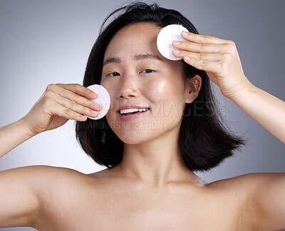 Buy stock photo Shot of a young woman using a cotton wipe on her face against a grey background