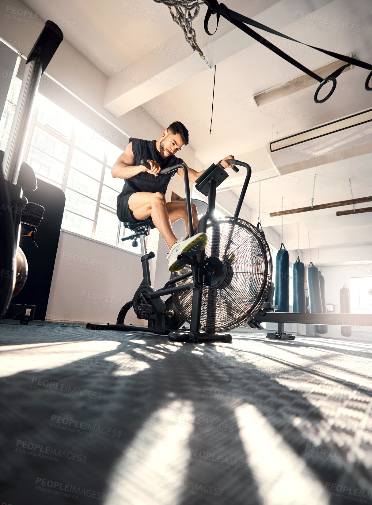 Buy stock photo Low angle shot of a sporty young man working out on an exercise bike in a gym