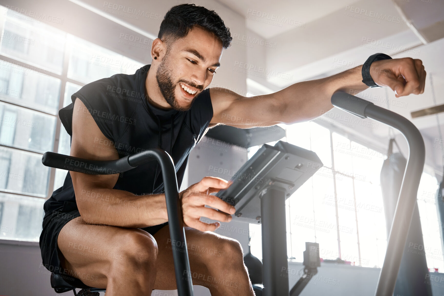 Buy stock photo Low angle shot of a sporty young man working out on an exercise bike in a gym