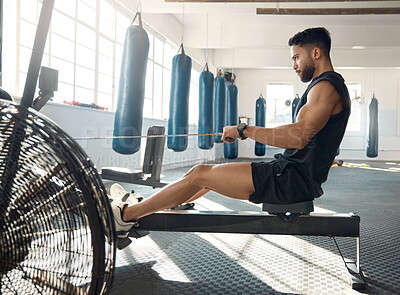 Buy stock photo Shot of a sporty young man exercising on a rowing machine in a gym