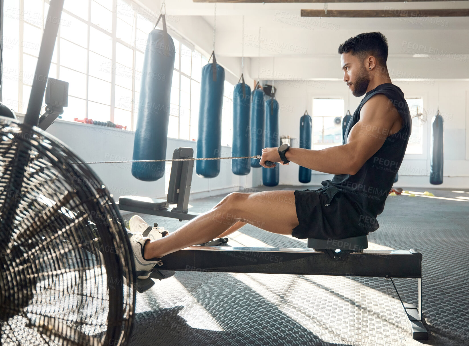 Buy stock photo Shot of a sporty young man exercising on a rowing machine in a gym