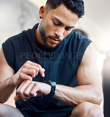 Buy stock photo Shot of a sporty young man checking his watch while exercising in a gym