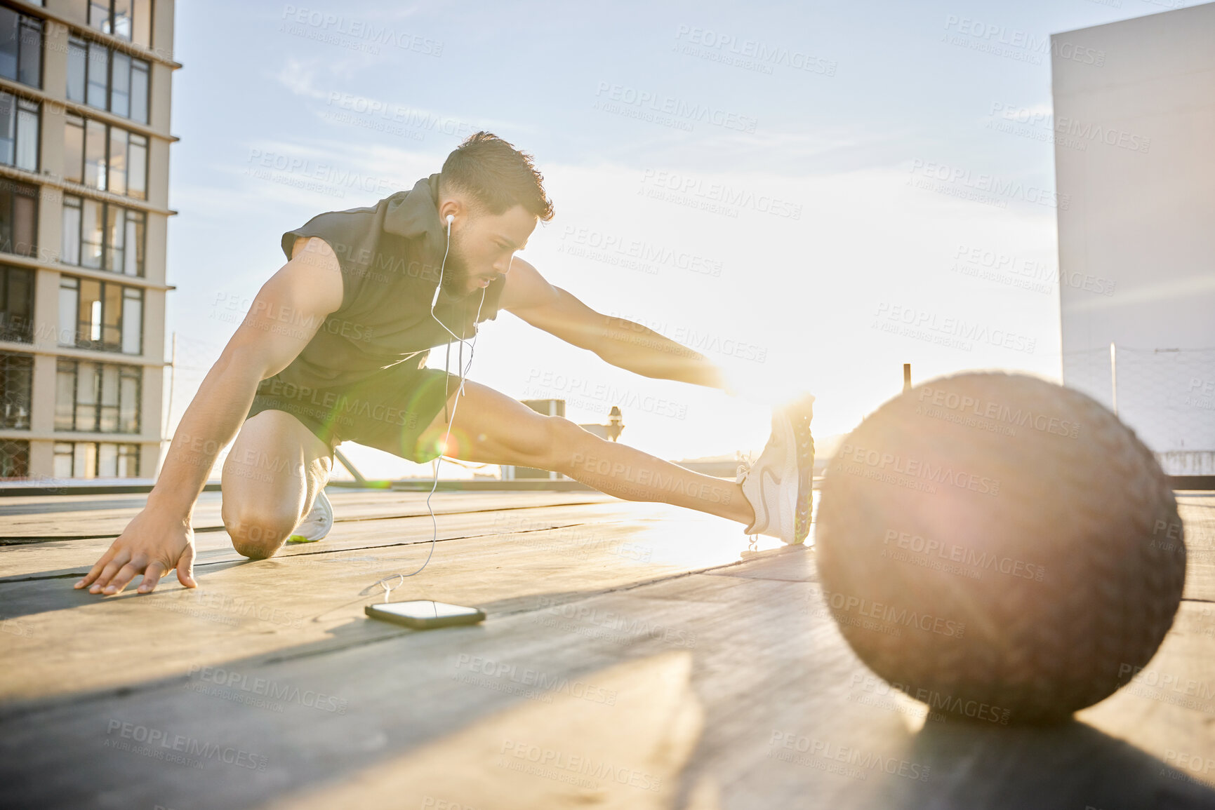 Buy stock photo Shot of a sporty young man stretching while out on a rooftop