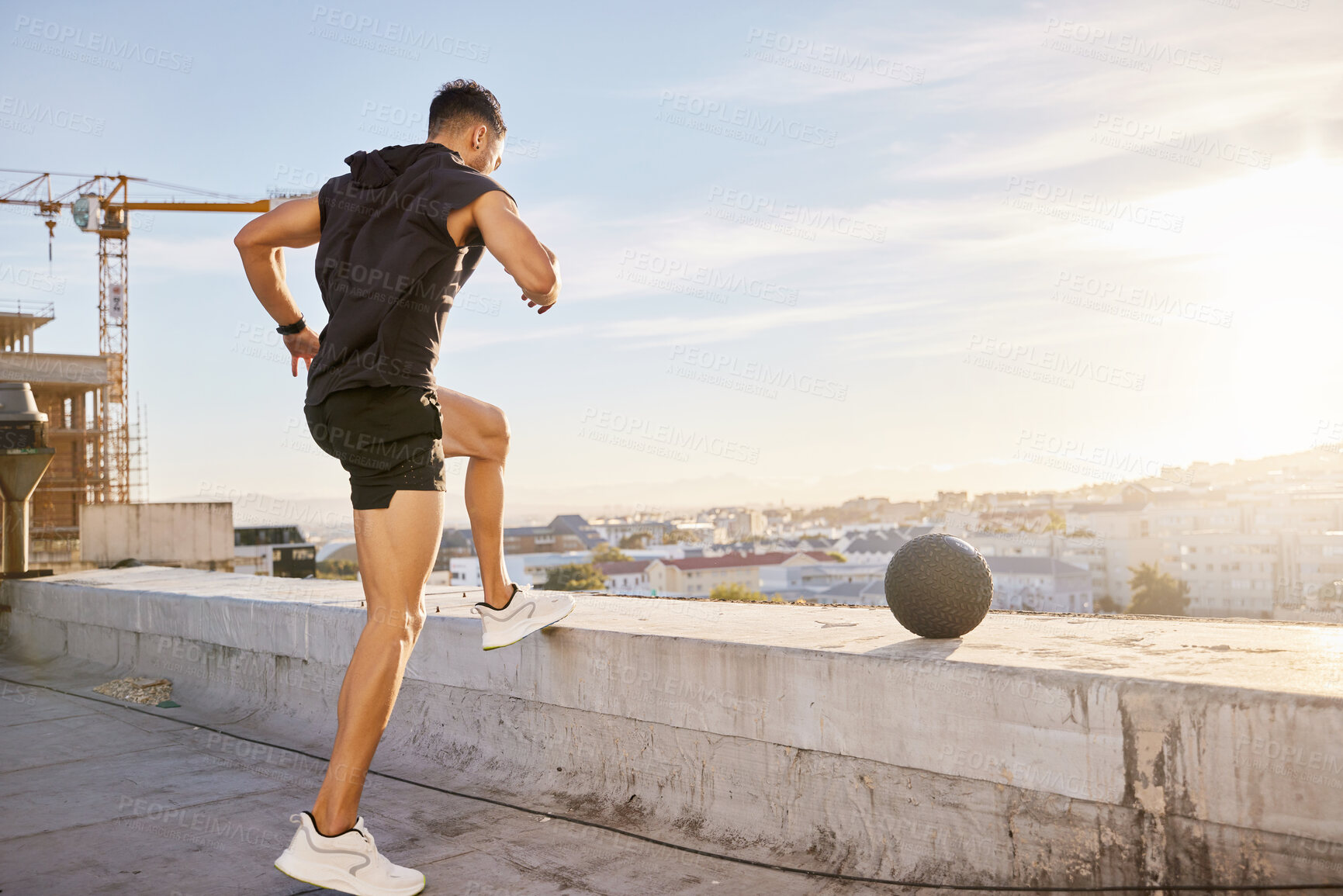 Buy stock photo Shot of a sporty young man out on a rooftop for a workout