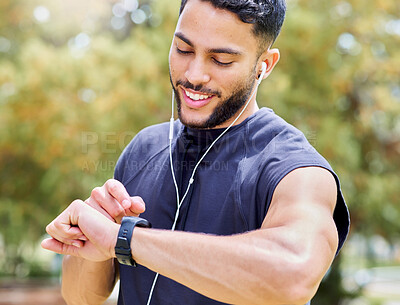 Buy stock photo Shot of a sporty young man listening to music and checking his watch while exercising outdoors