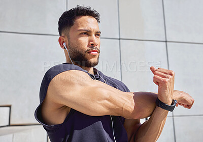 Buy stock photo Shot of a sporty young man listening to music and stretching his arms while exercising outdoors