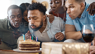 Buy stock photo Shot of a young man blowing out his birthday candles at his party at home