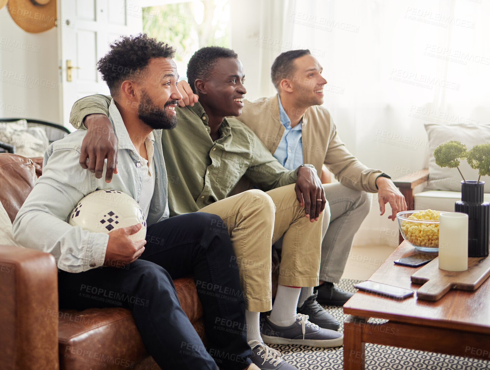 Buy stock photo Shot of three male friends watching something together while sitting on a couch