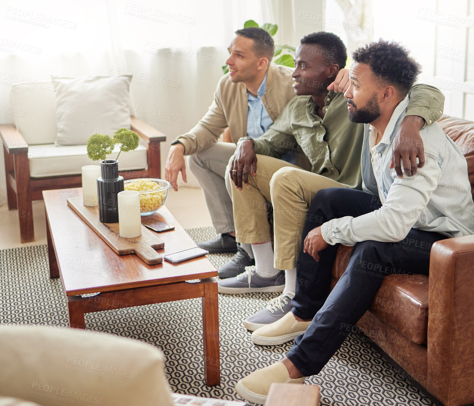 Buy stock photo Shot of three male friends watching something together while sitting on a couch