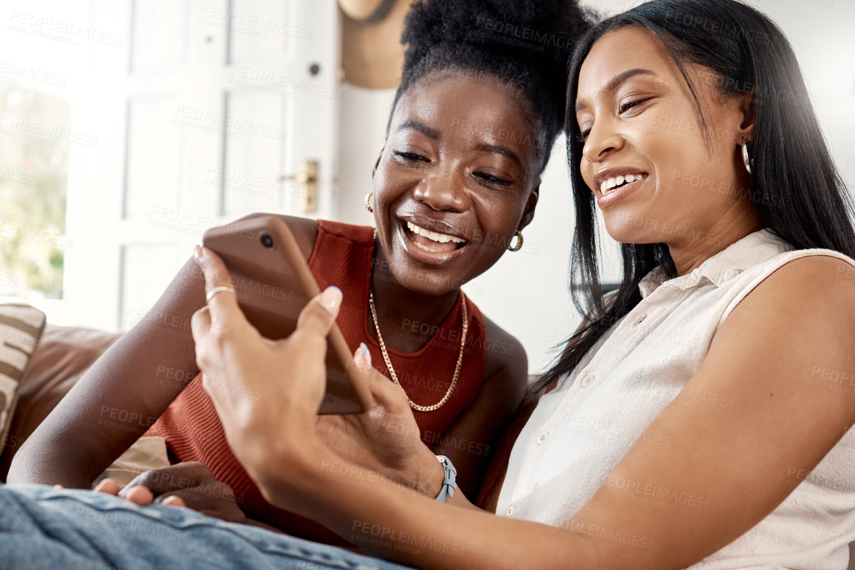 Buy stock photo Shot of two young friends using a phone while spending time together at home