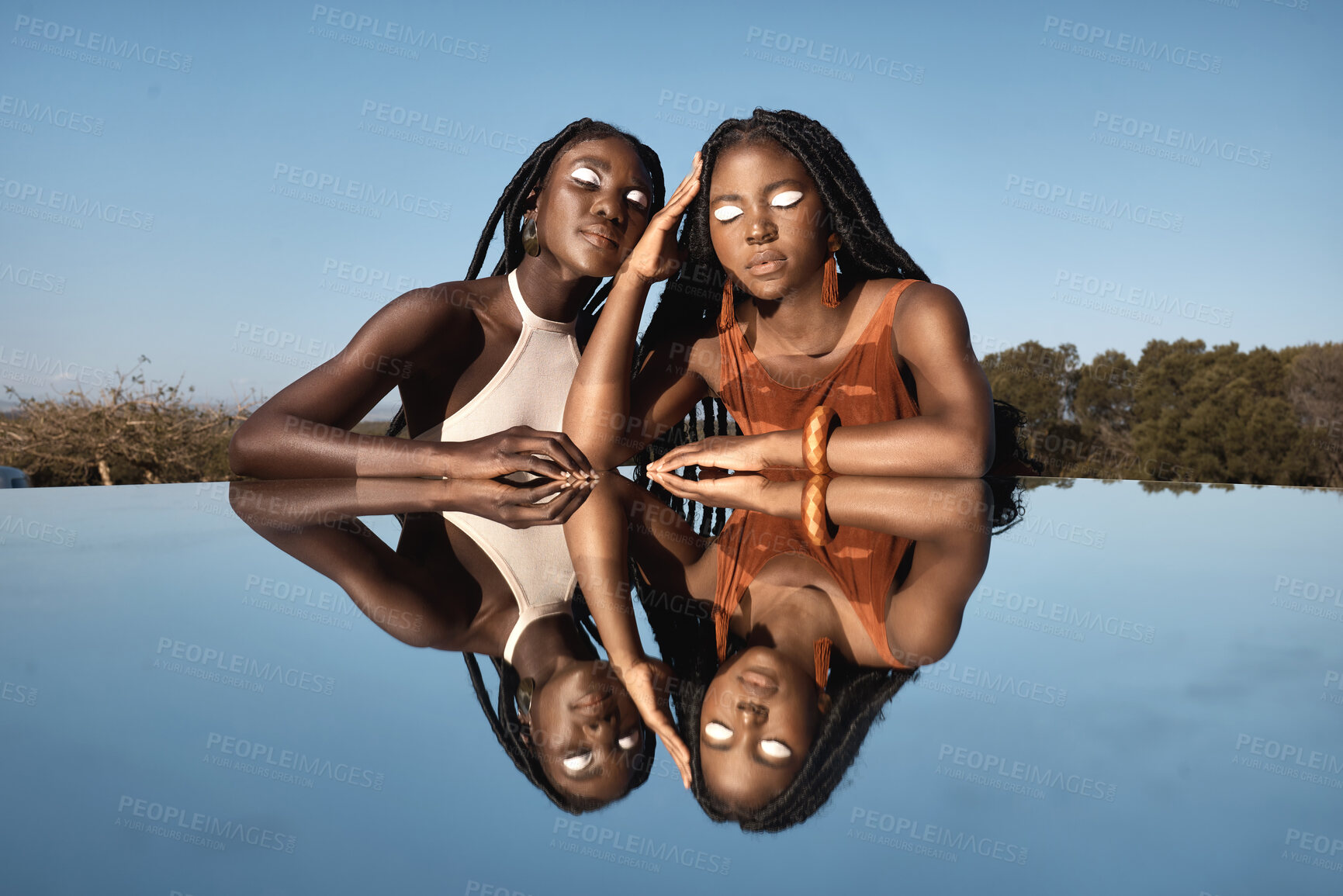 Buy stock photo Shot of two attractive young women sitting next to a pond with their reflection in it in nature