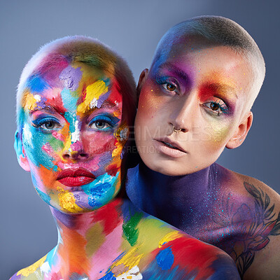 Buy stock photo Studio shot of two young women posing with multi-coloured paint on her face