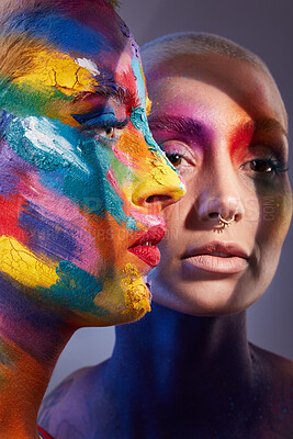 Buy stock photo Studio shot of two young women posing with multi-coloured paint on her face