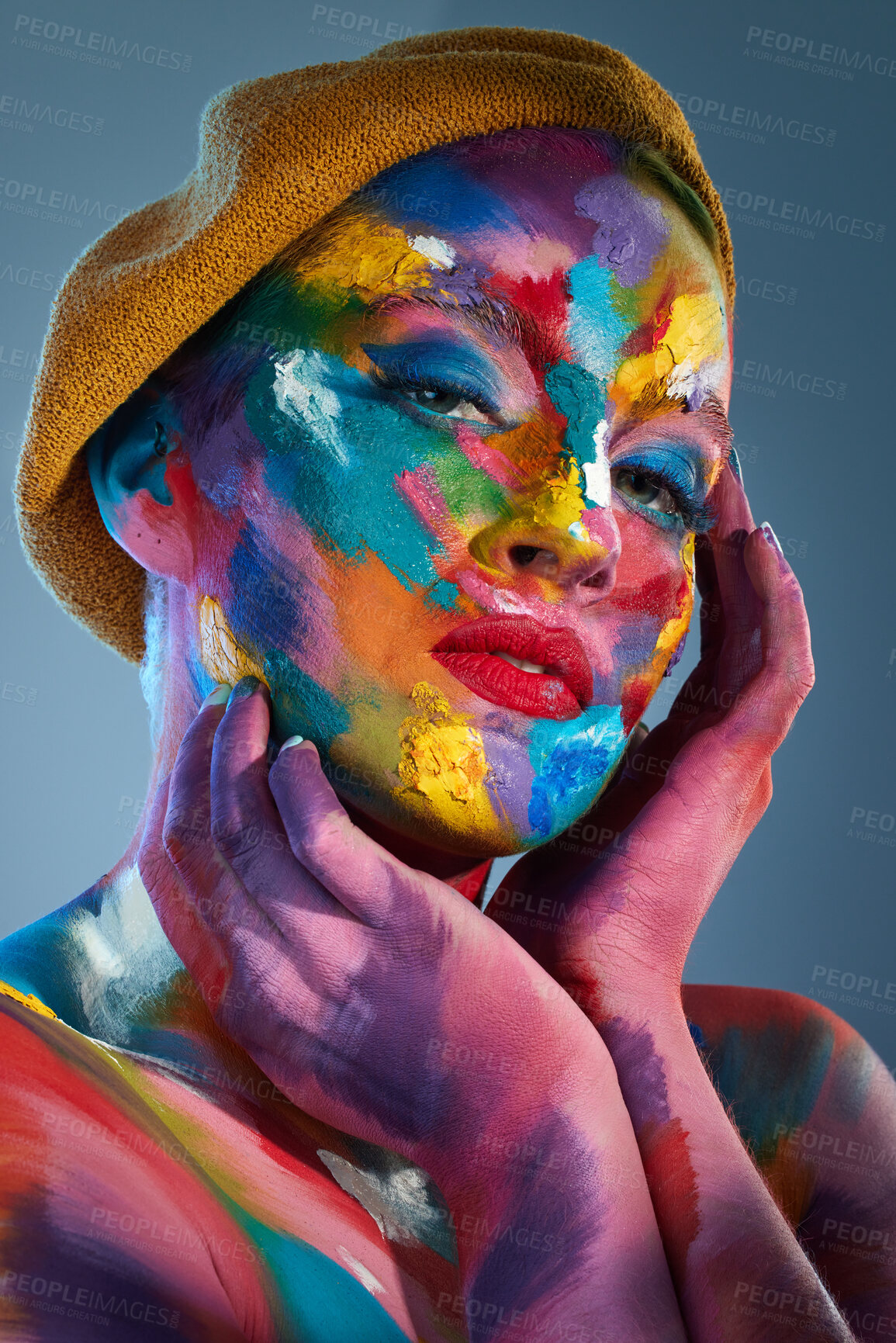 Buy stock photo Studio shot of a young woman posing with multi-coloured paint on her face and a french hat on her head