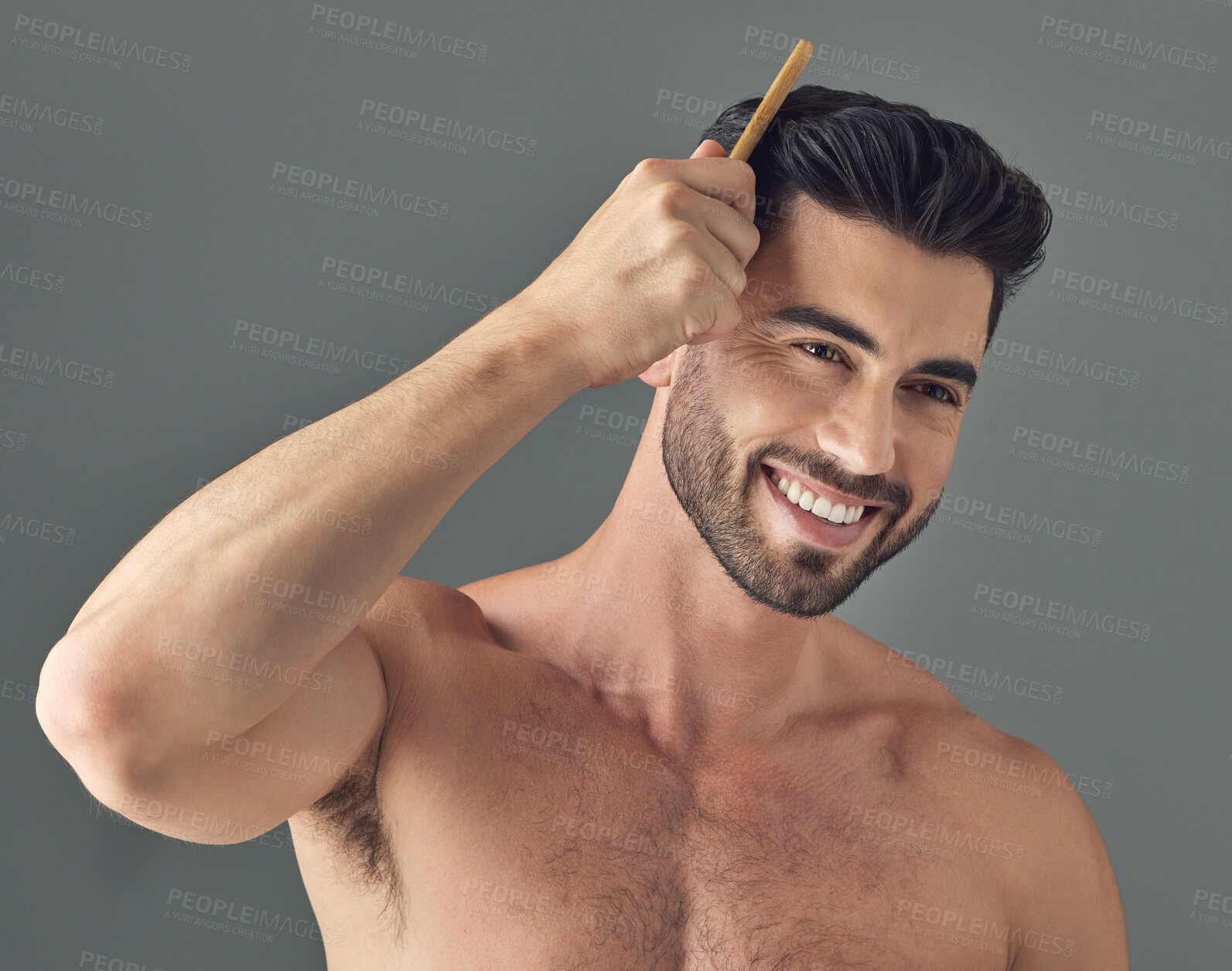 Buy stock photo Shot of a handsome young man combing his hair while standing against a grey background