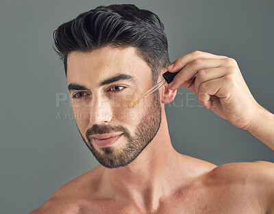 Buy stock photo Shot of a handsome young man applying serum to his face with a dropper