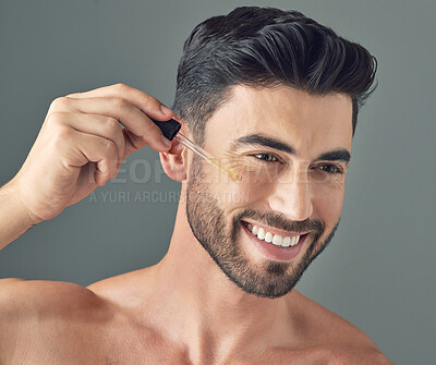 Buy stock photo Shot of a handsome young man applying serum to his face with a dropper