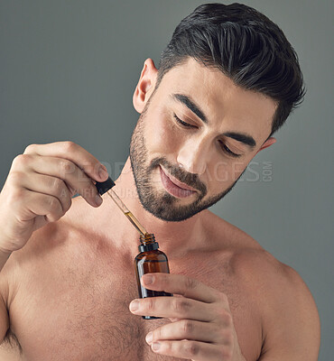 Buy stock photo Shot of a handsome young man applying serum to his face with a dropper