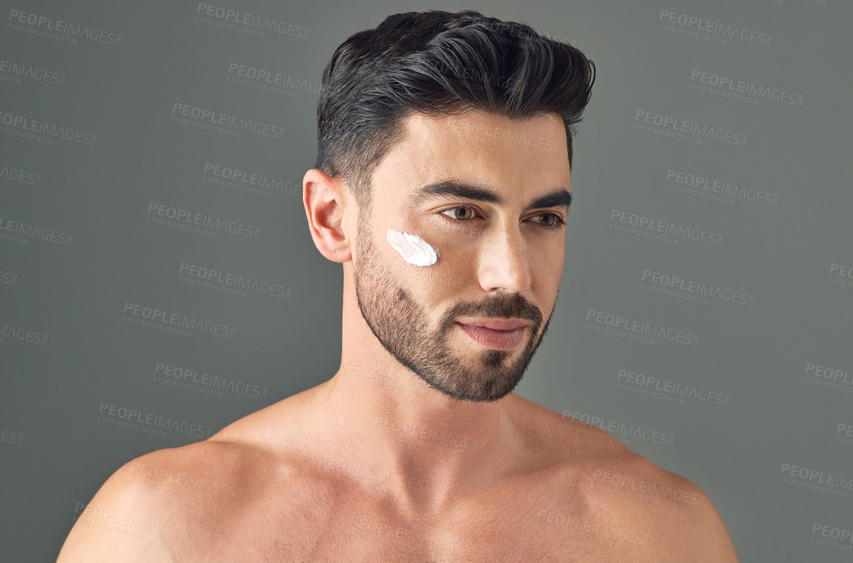 Buy stock photo Studio shot of a handsome young man posing with moisturiser on his face