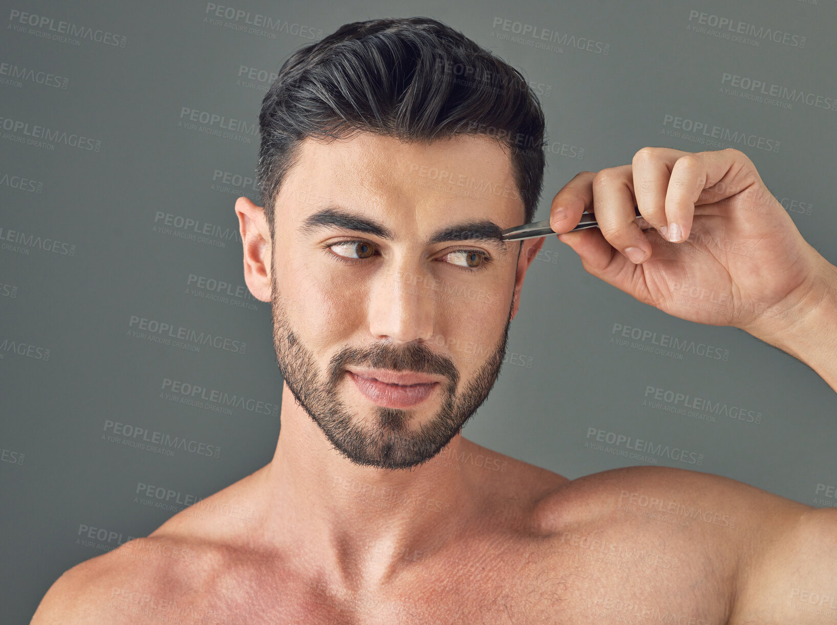 Buy stock photo Shot of a handsome young man tweezing his eyebrows