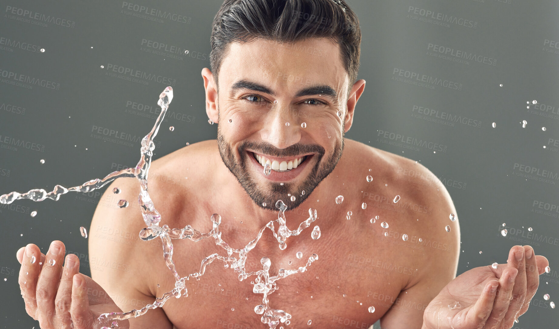 Buy stock photo Shot of a handsome young wan washing his face while standing against a grey background