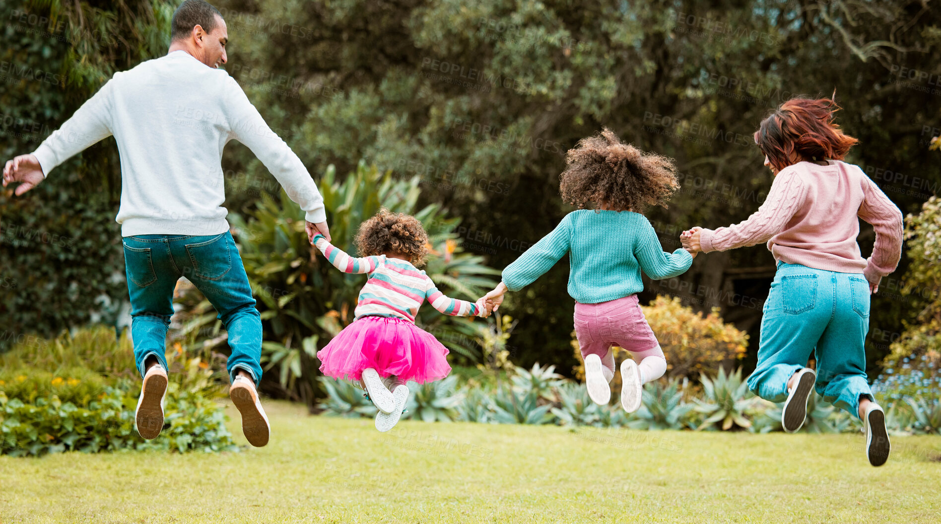 Buy stock photo Family, jump and holding hands at park with back, link and support with love, bonding and game on lawn. Parents, children and outdoor in garden with connection, learning or trust on grass in Colombia