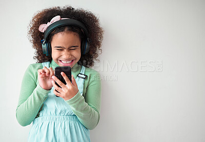 Buy stock photo Girl, white background and happy on smartphone with headphones for streaming music or playlist. Kid, audio and excited or smile on internet, online and mobile app for entertainment on mockup space