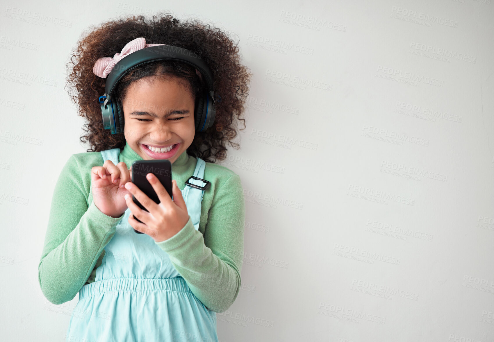 Buy stock photo Girl, white background and happy on smartphone with headphones for streaming music or playlist. Kid, audio and excited or smile on internet, online and mobile app for entertainment on mockup space