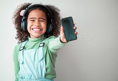 Buy stock photo Girl, white background and smartphone screen with headphones for streaming music or playlist. Kid, audio and excited or happy for promotion, advertising and mobile app for subscribers with mockup