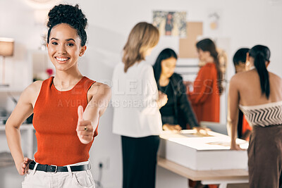Buy stock photo Shot of a young woman showing the thumbs up while her coworkers collaborate in the background