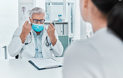 Buy stock photo Shot of a mature doctor putting a face mask on during a consultation with his patient in the clinic