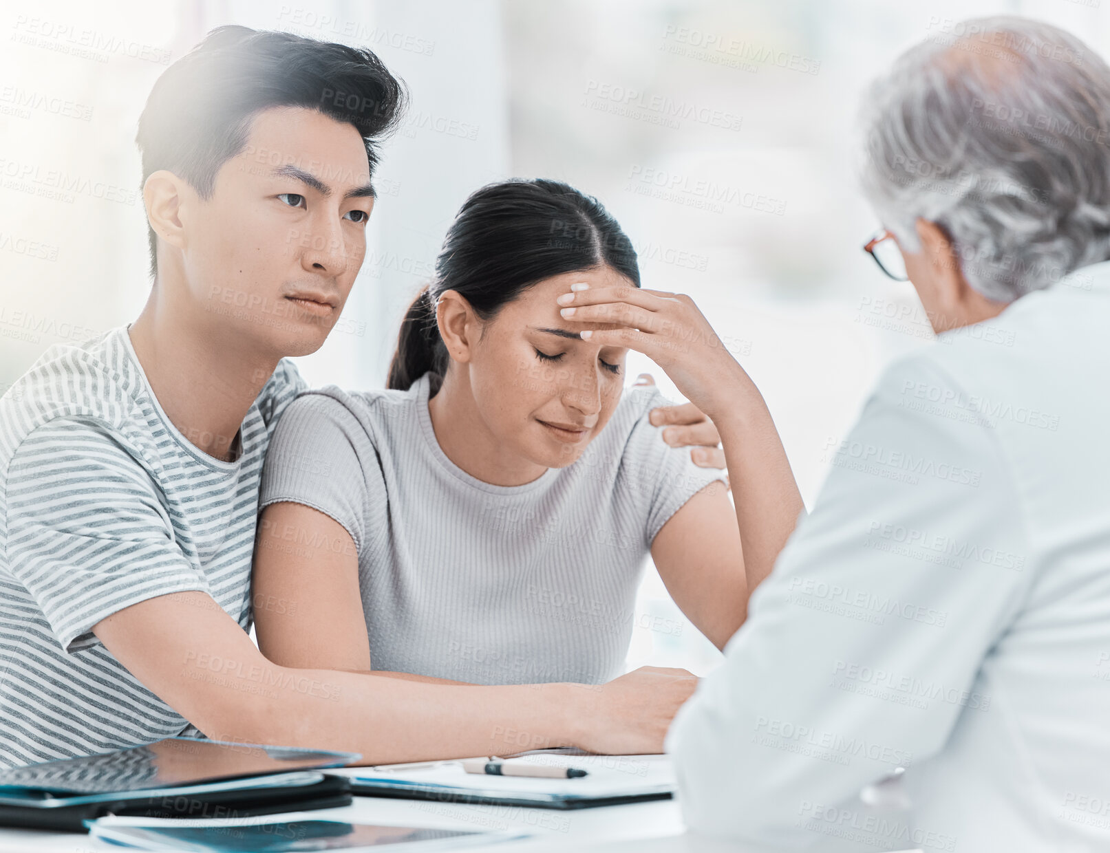Buy stock photo Shot of a young couple sitting with their doctor and looking upset during a consultation in the clinic