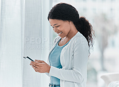 Buy stock photo Shot of an attractive young woman standing alone in the clinic and using her cellphone