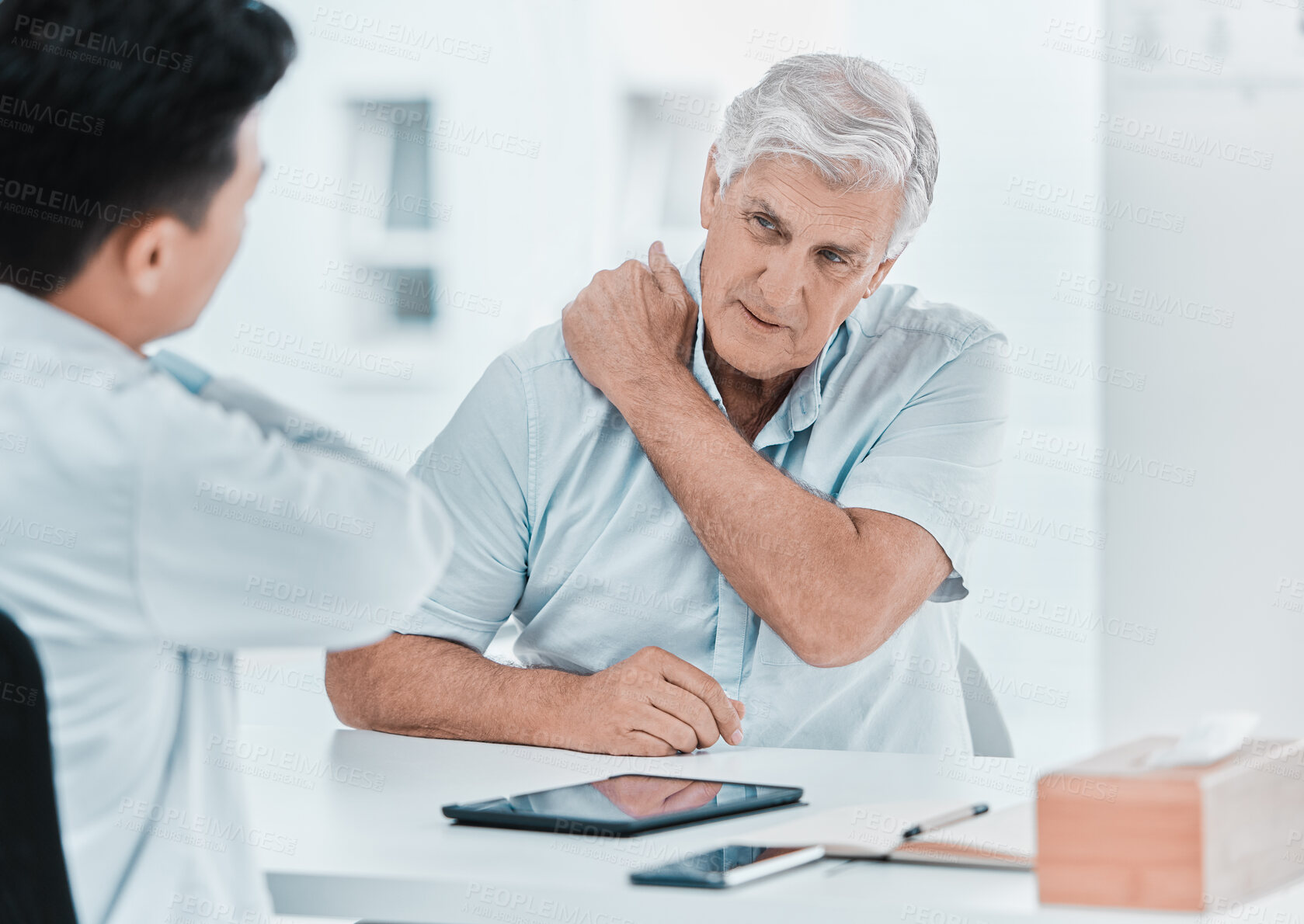 Buy stock photo Shot of a mature man sitting with his doctor and complaining about a sore shoulder during a consultation