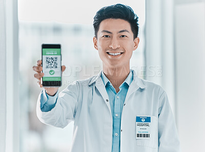 Buy stock photo Shot of a handsome young doctor standing alone in the clinic and showing his Covid passport on his cellphone