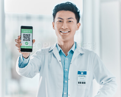 Buy stock photo Shot of a young doctor standing alone in the clinic and showing his Covid passport on his cellphone